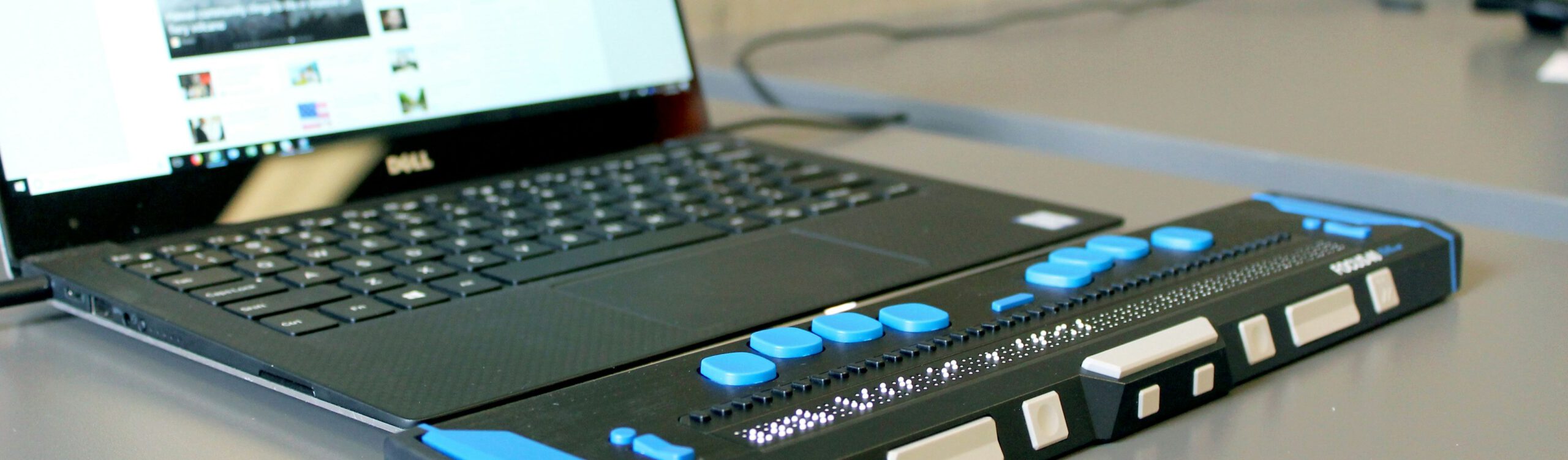 Ein Laptop mit einer angeschlossenen Braillezeile für blinde Menschen steht auf einem Schreibtisch